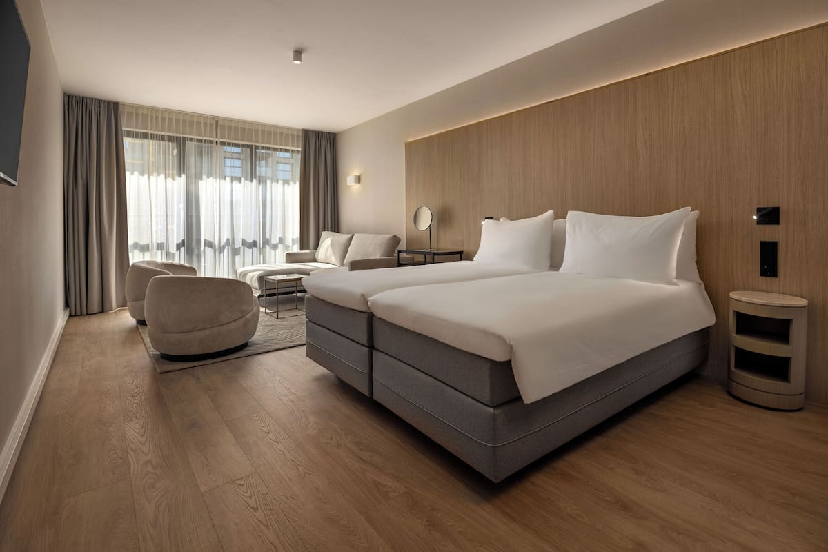 A modern hotel room with a large bed, two armchairs, a small table, and a side table.