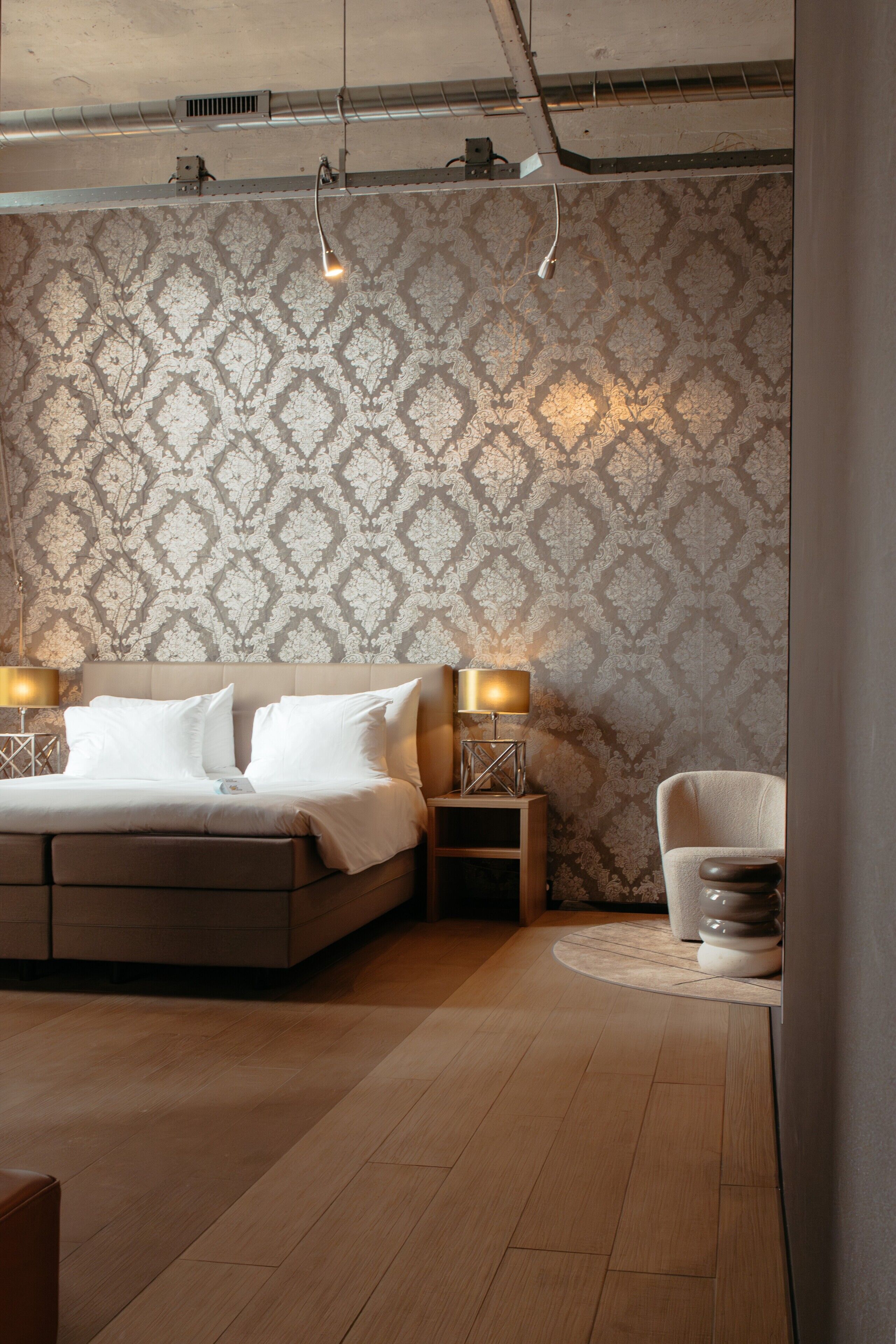 A bedroom with a bed, two bedside tables, a chair, and a patterned wallpaper.
