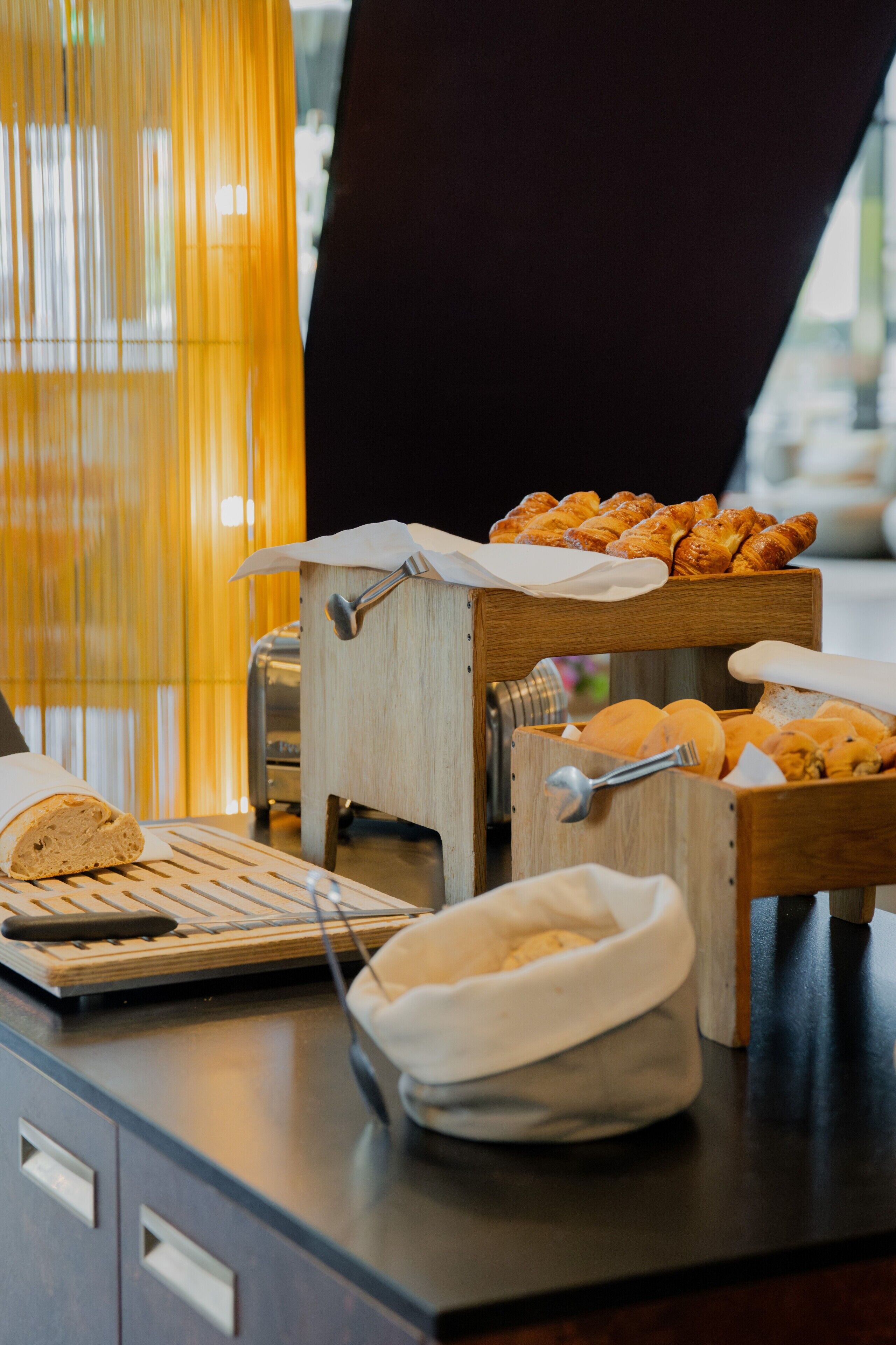 A breakfast buffet with bread, pastries, and a bread slicer.