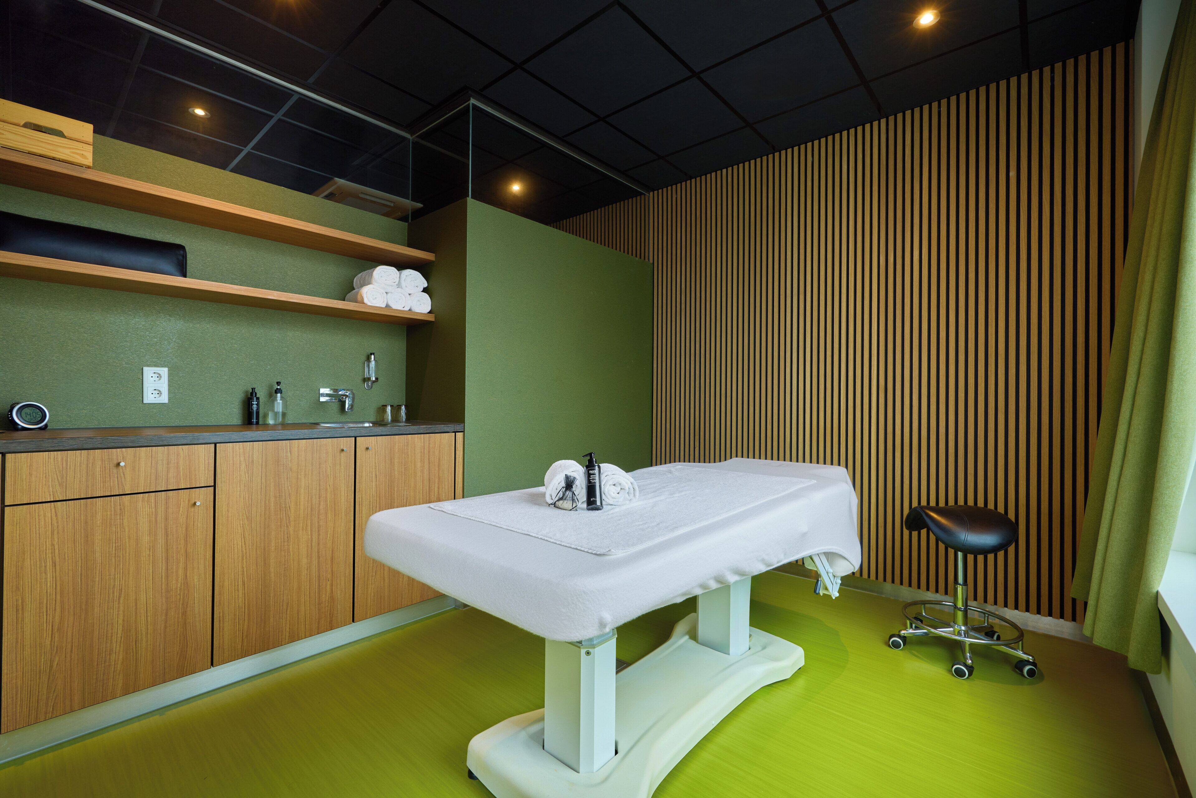 A medical examination room with a treatment table, a stool, wooden cabinets, and a green wall.