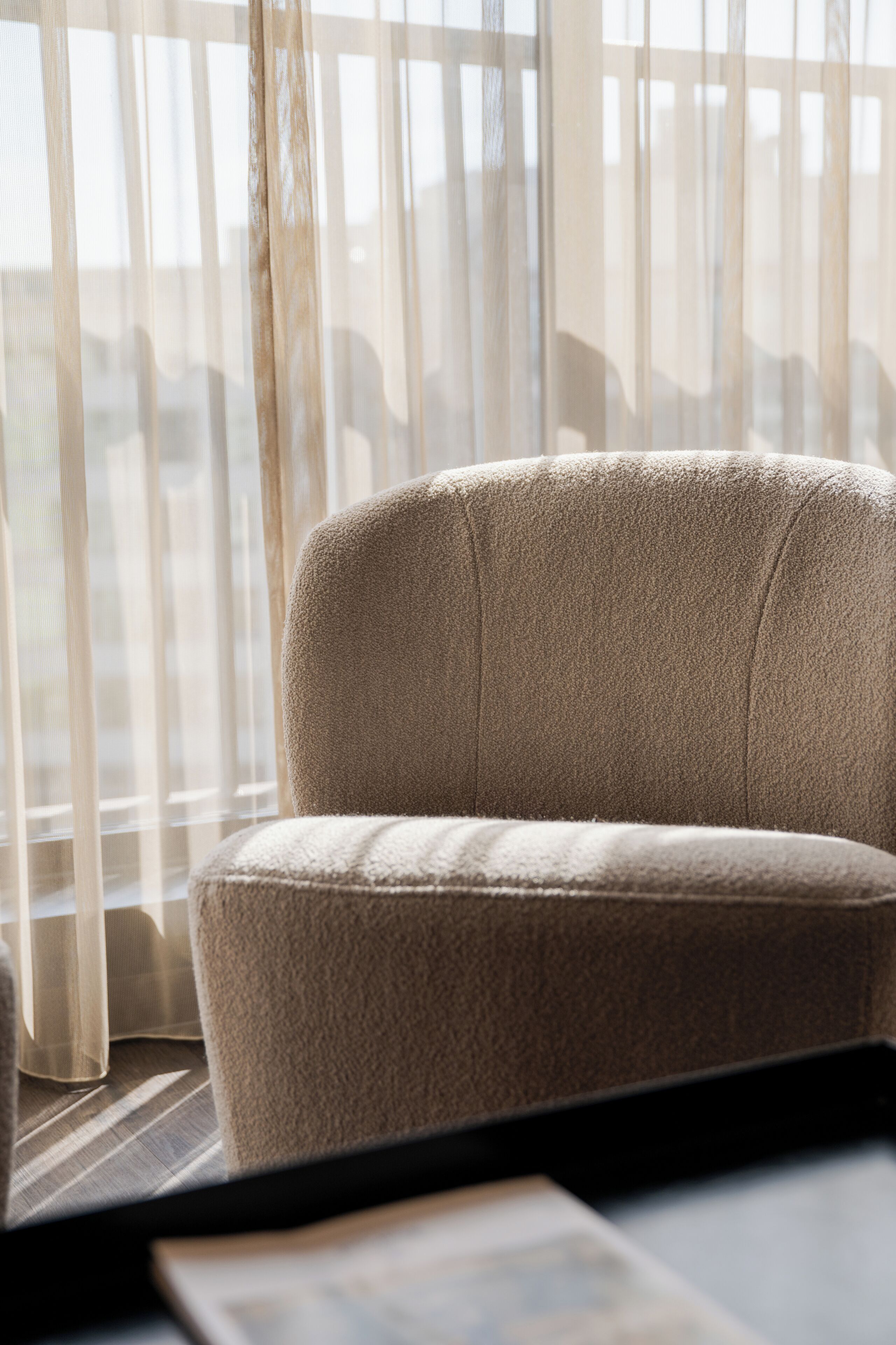 Ein Sofa vor einem Fenster mit durchscheinenden Vorhängen, durch das natürliches Licht in den Raum fällt.