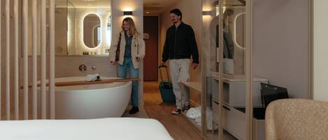 A modern hotel room with a large bathtub, a walk-in closet, and a mirror with lights.