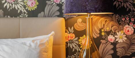 A neatly made bed with white linens, a dark blue lampshade, and a wooden nightstand with a vase.