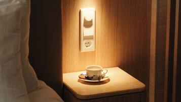 Een hotelkamer met een net opgemaakt bed, een nachtkastje met een kop koffie, en een wandlamp.