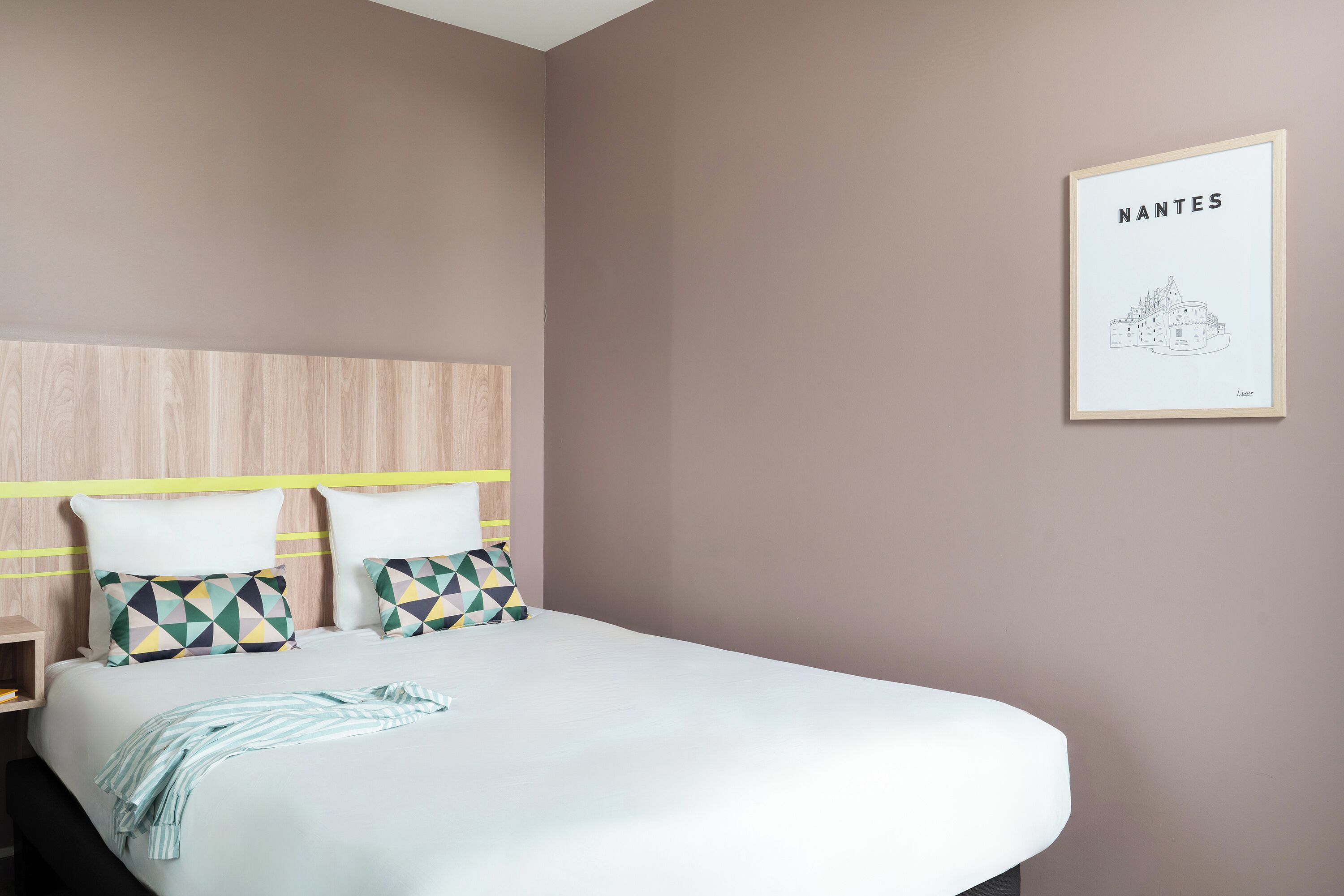A bedroom with a bed, two pillows, a bedside table, and a wall-mounted artwork.