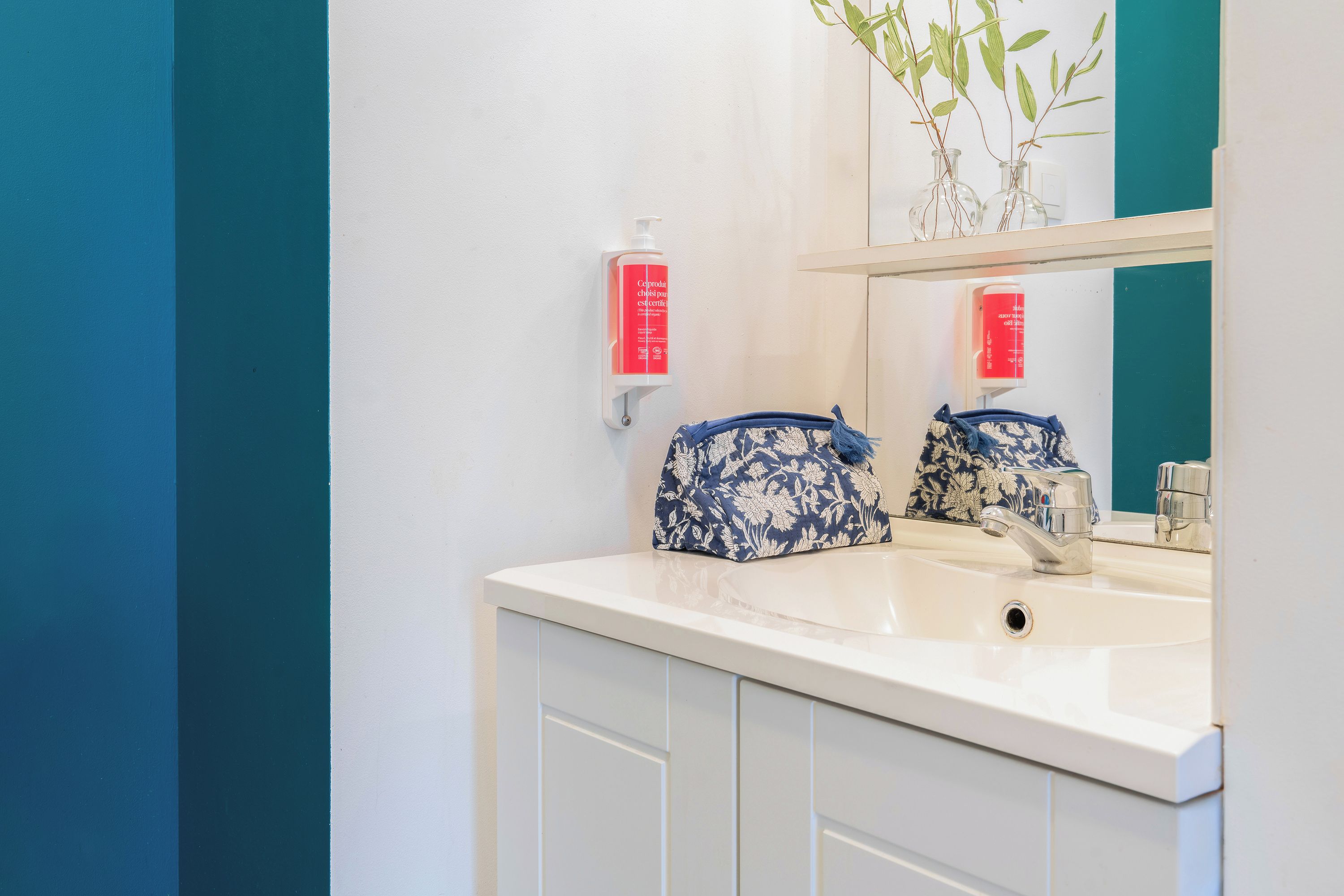 A bathroom with a white sink, a mirror, and a blue and white patterned bag on the counter.