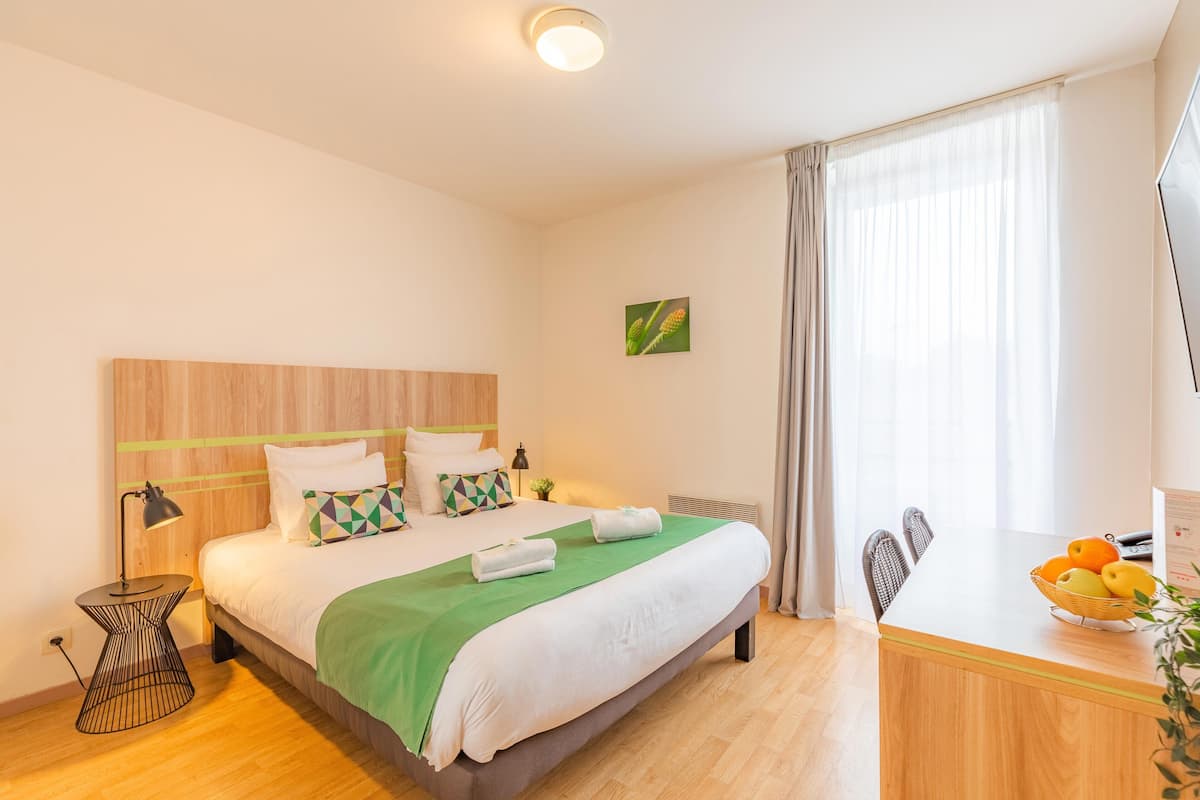 Una habitación de hotel con cama, mesita de noche, lámpara y escritorio con frutero.
