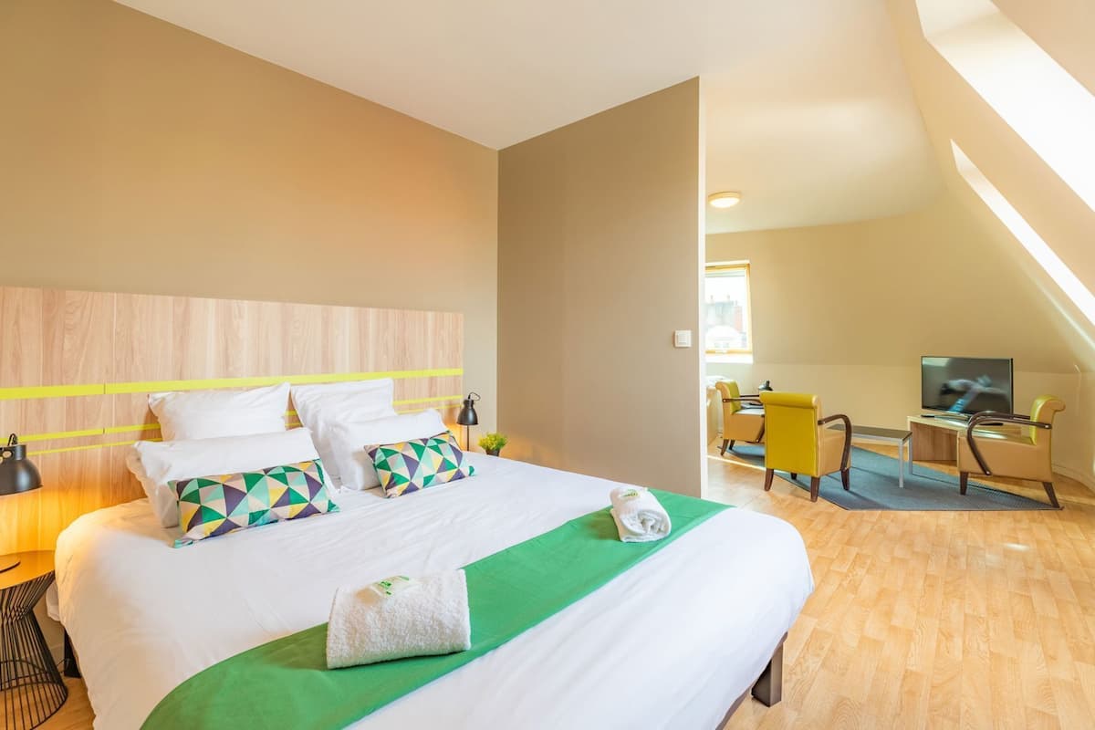 Una habitación de hotel con cama, escritorio, silla, televisor y ventana.