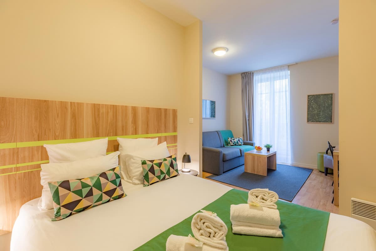 Una habitación de hotel con cama, sofá, una mesita y una silla.