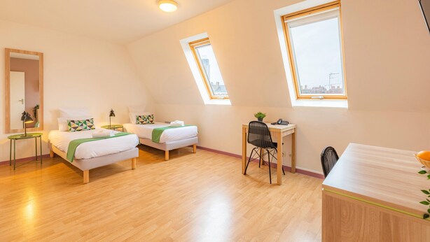 Een moderne, goed verlichte kamer met een slaapverdieping, een bureau en een stoel. Twee ramen bieden daglicht en uitzicht op de stad.