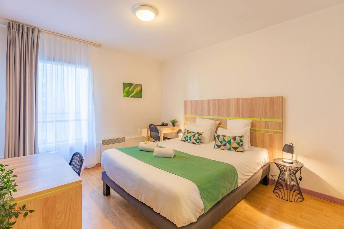 Una habitación de hotel con cama, escritorio, silla, mesita de noche y lámpara.