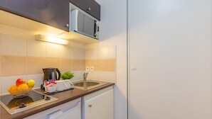 Een compacte keuken met een ingebouwde magnetron, een koffiezetapparaat, een spoelbak en een kleine koelkast.