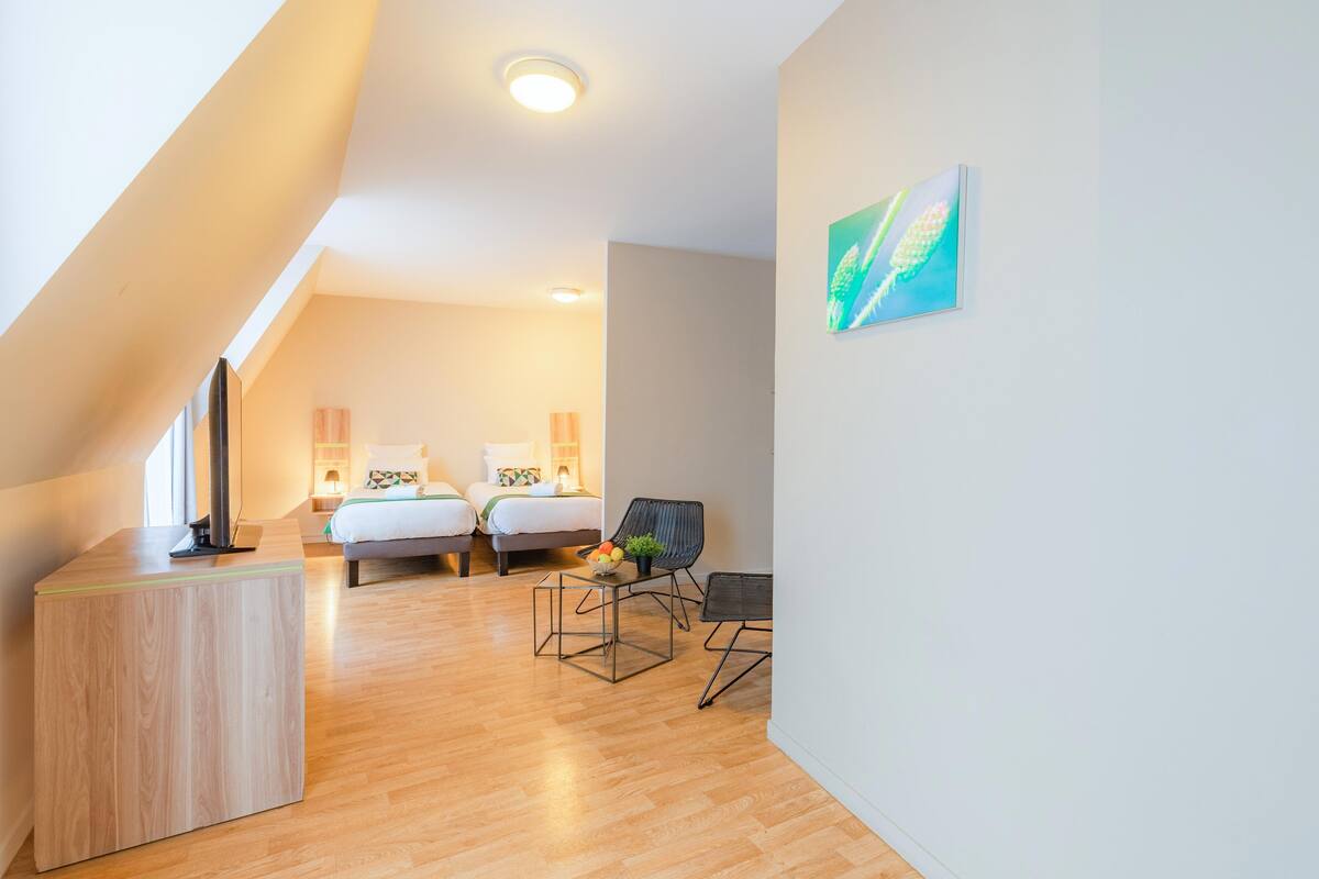 Una habitación moderna y luminosa, con suelo de madera, un escritorio, dos camas y una silla.