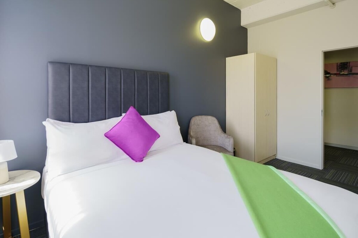 Una habitación de hotel con cama, una silla, escritorio y armario.