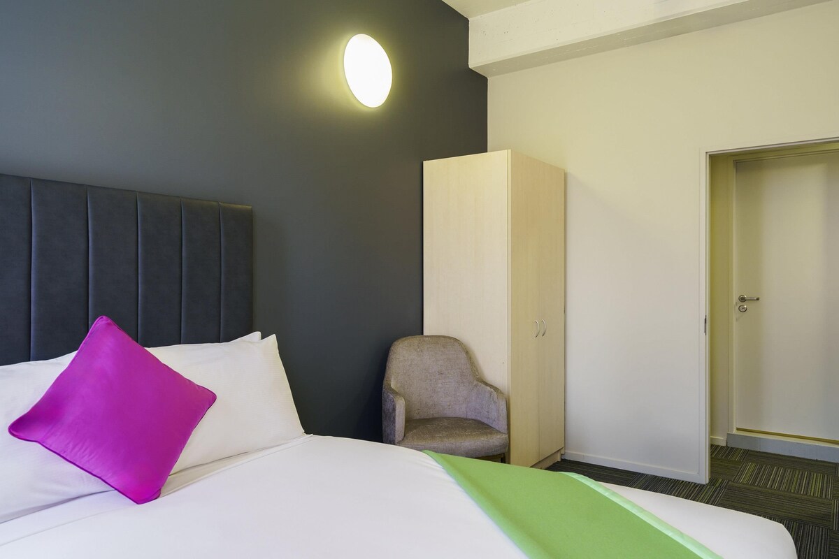 Una habitación de hotel con cama, una silla, un armario y una puerta.