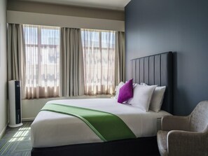 A hotel room with a bed, a chair, a window with curtains, and a wall unit.