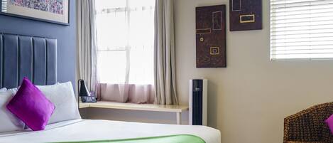 Una habitación de hotel con una cama, una ventana con cortinas, una silla y obras de arte en las paredes.