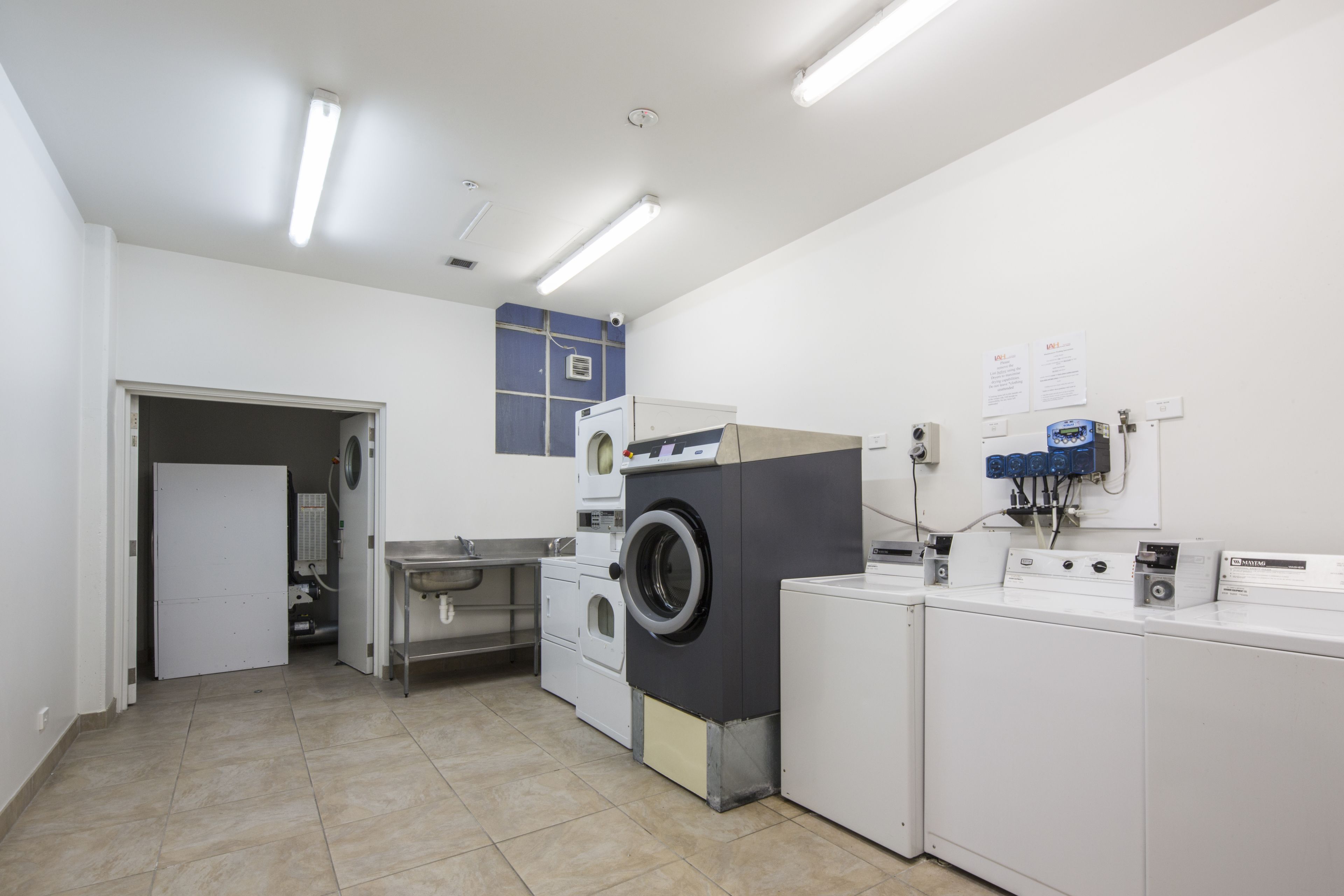 A laundry room with multiple washing machines, a drying machine, and a sink.