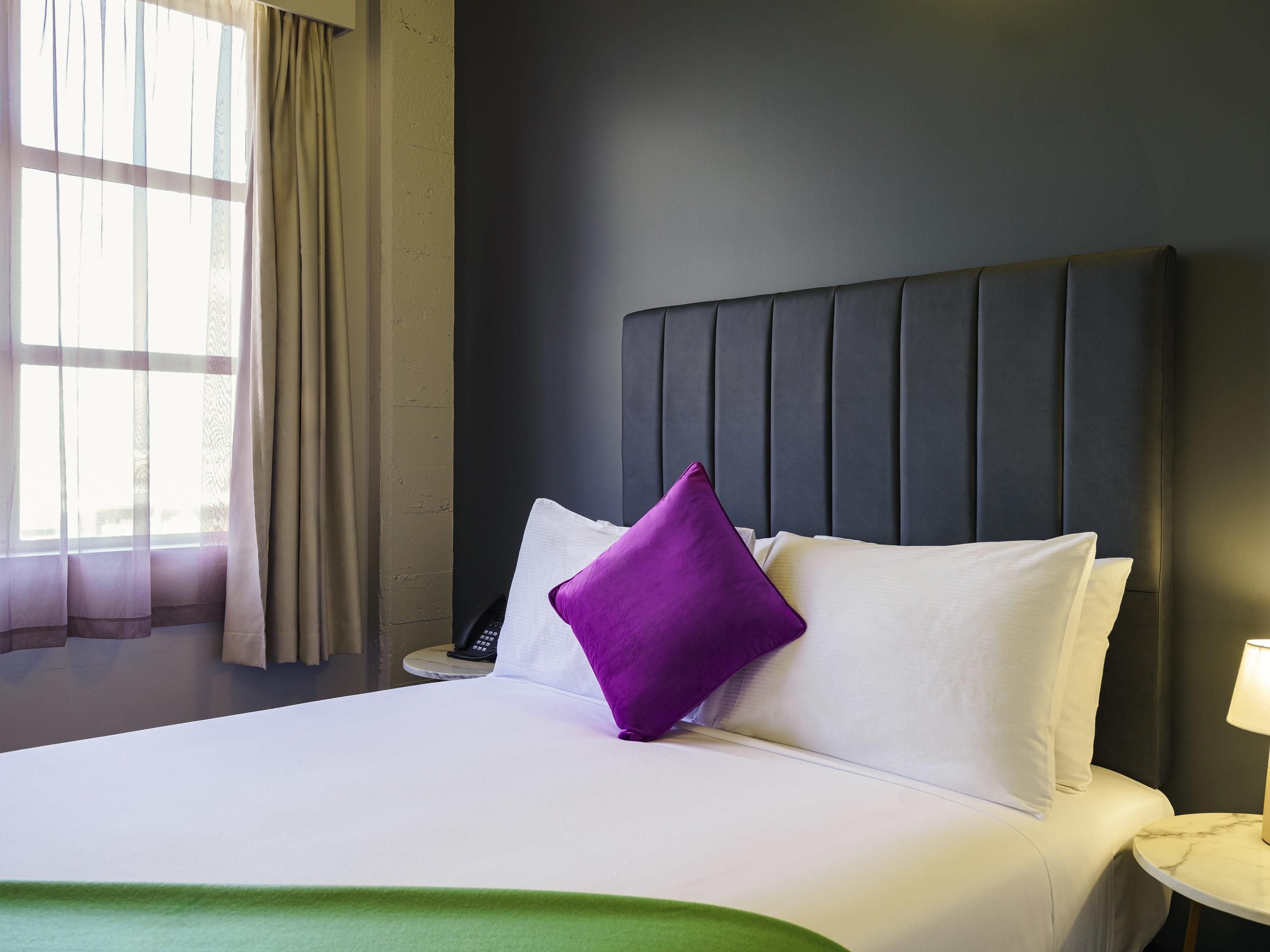 A hotel room with a bed, a nightstand, a lamp, and a window with curtains.
