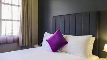 A hotel room with a bed, a nightstand, a lamp, and a window with curtains.
