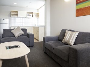 Ein modernes Wohnzimmer mit zwei grauen Sofas, einem kleinen runden Tisch und einer Küche im Hintergrund.
