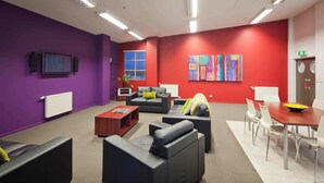 Un espacio de oficina moderno con paredes moradas y rojas, sofás de cuero, una mesa de madera y un ventanal grande.