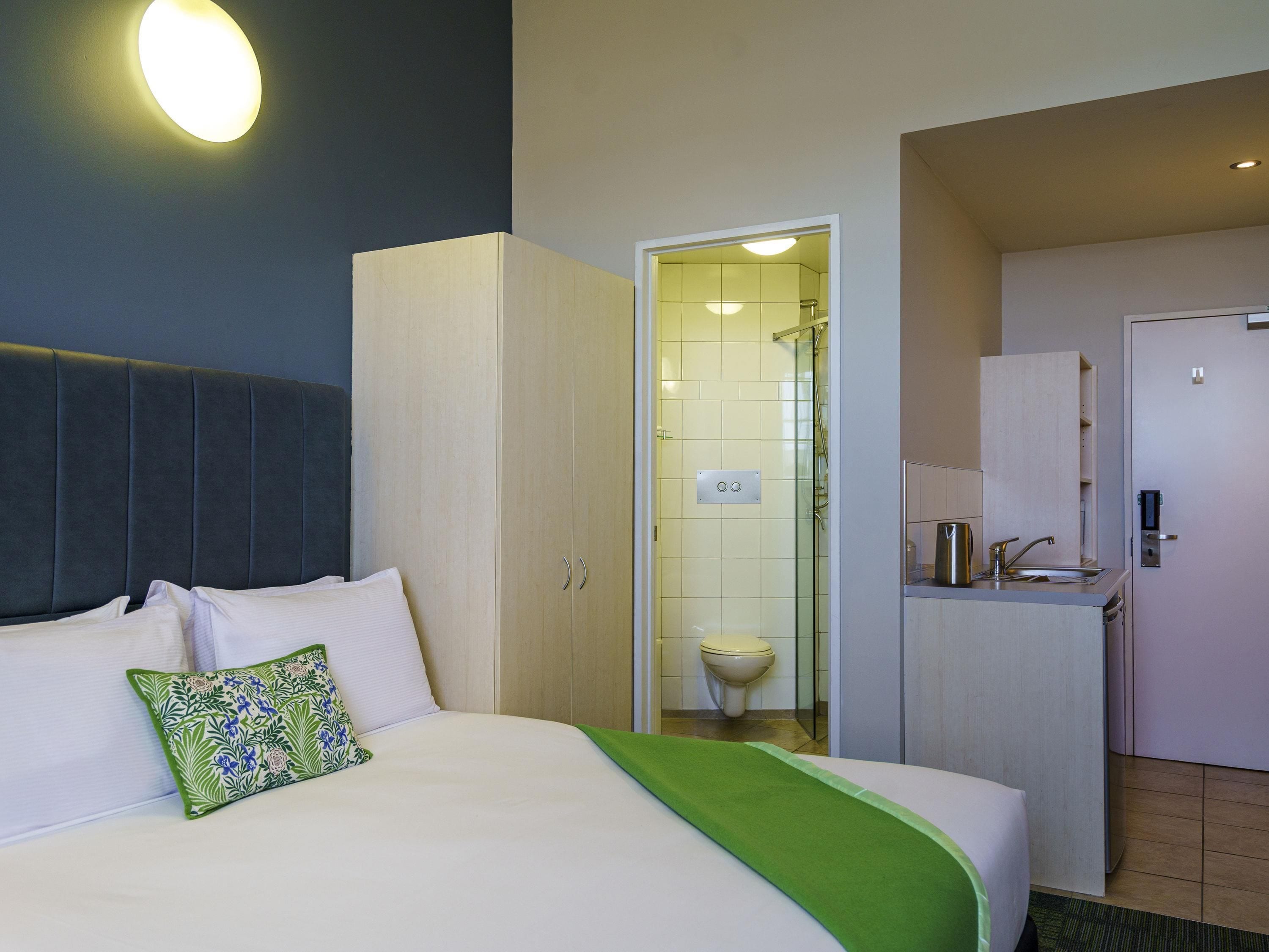 A hotel room with a bed, a bathroom, and a kitchenette.