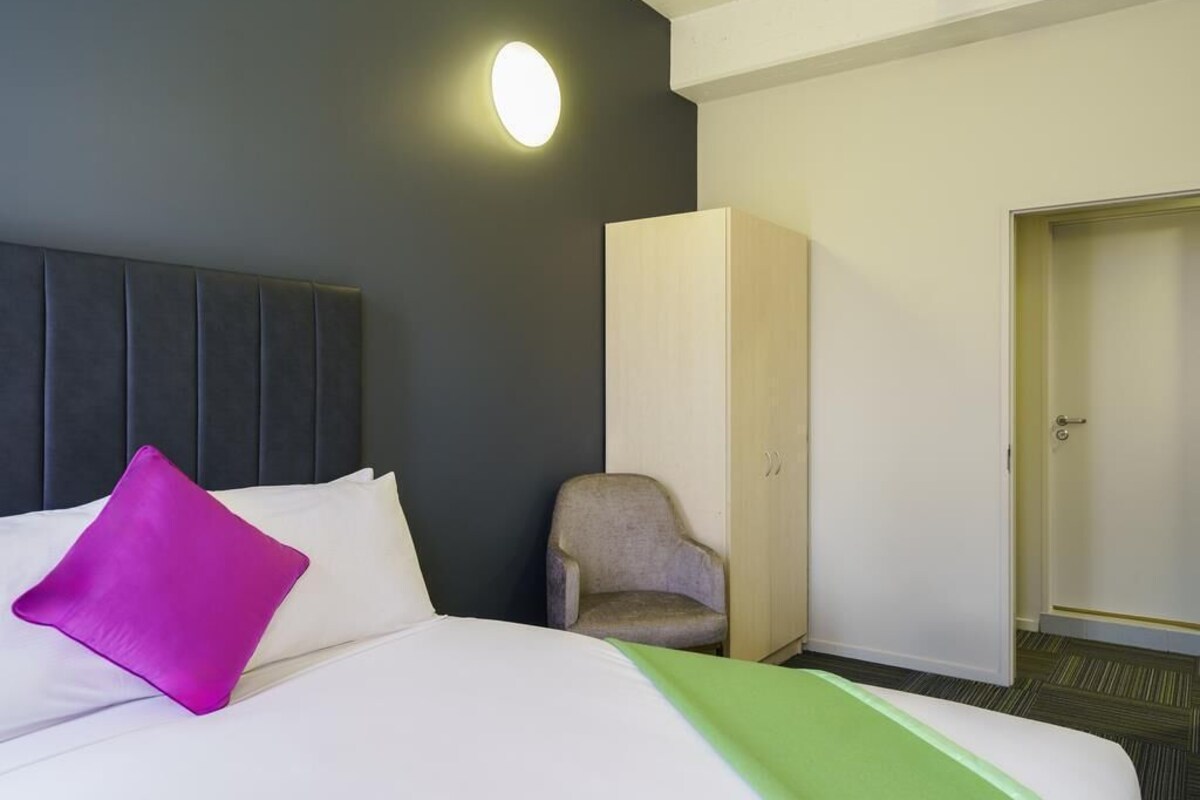 Una habitación de hotel con cama, una silla, un armario y una puerta.