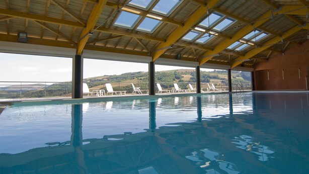 An indoor swimming pool with a high ceiling, skylights, and a view of hills. - Madame Vacances Residence La Marquisié (Trebas)