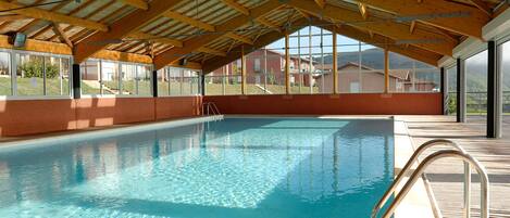 An indoor swimming pool with a wooden ceiling and large windows.