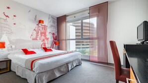 A hotel room with a large bed, a desk with a computer, a window with a view of buildings, and a wall with a mural. - Lagrange Apart'HOTEL Strasbourg Wilson (Strasbourg)
