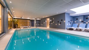 A modern indoor swimming pool with clear blue water, lounge chairs, and a tiled wall with geometric patterns. - Lagrange Apart'HOTEL Strasbourg Wilson (Strasbourg)