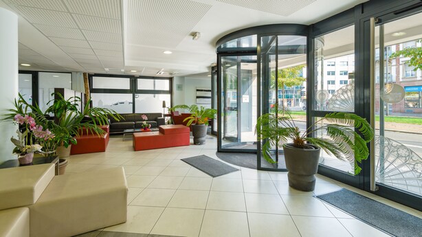 A modern lobby with a curved glass entrance, comfortable seating, and potted plants. - Lagrange Apart'HOTEL Strasbourg Wilson (Strasbourg)