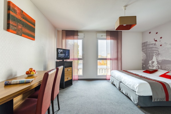 A hotel room with a bed, a desk with a chair, a television, and a window with curtains. - Lagrange Apart'HOTEL Strasbourg Wilson (Strasbourg)