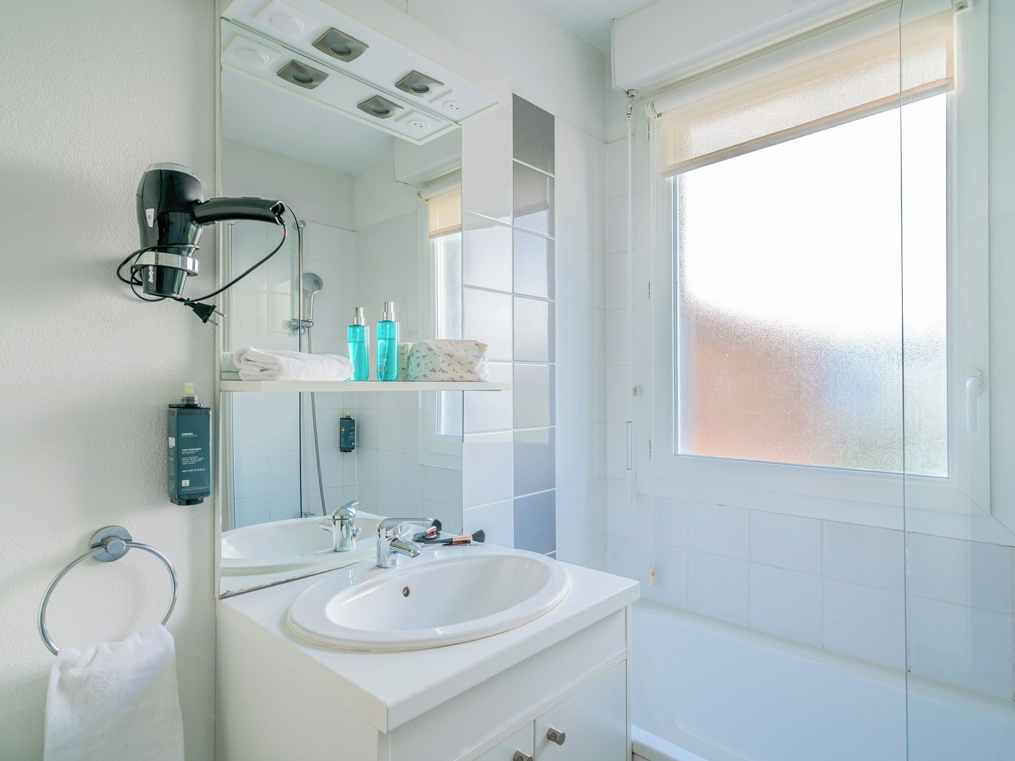 A modern bathroom with two sinks, a large mirror, a towel rack, and a window with frosted glass.