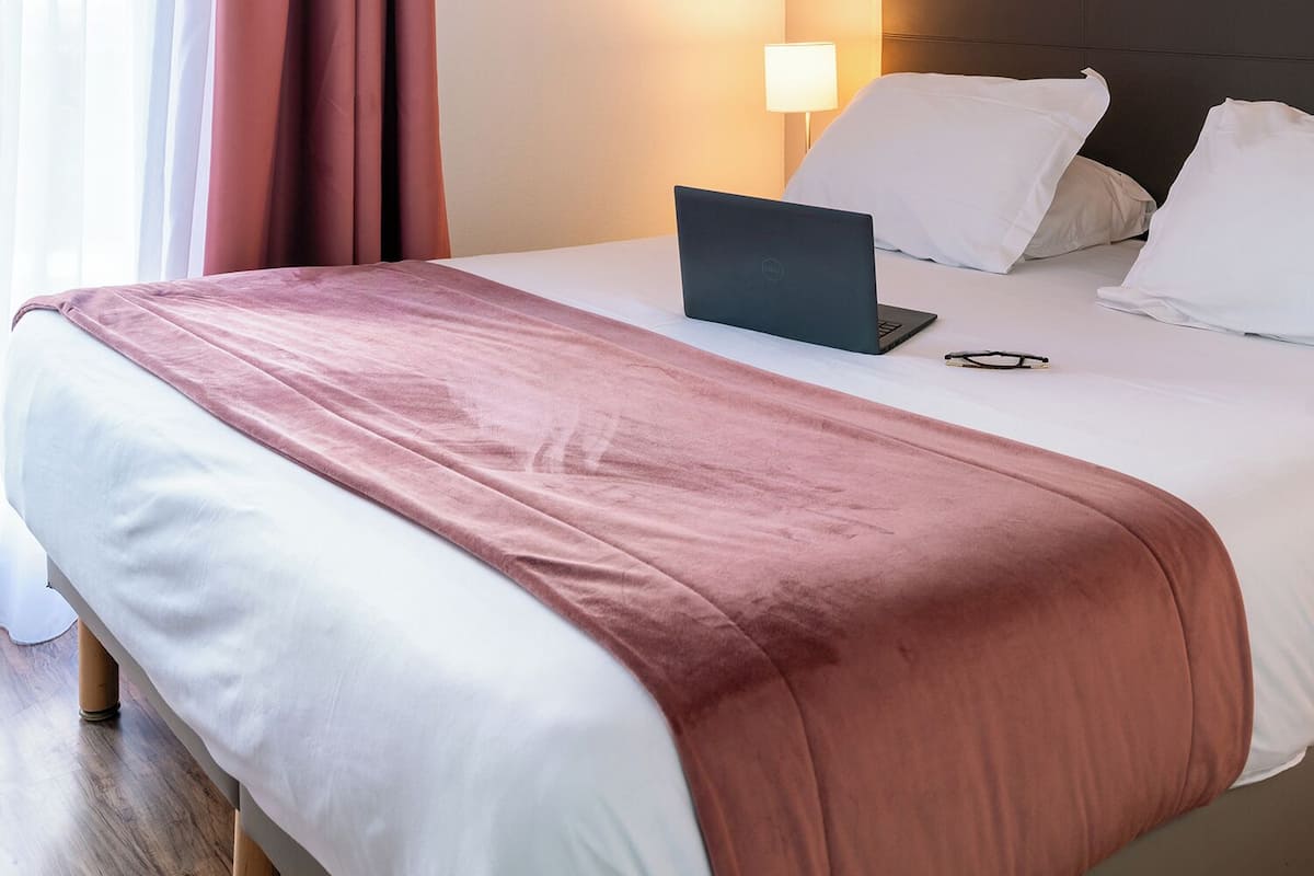 Ein Hotelzimmer mit einem Bett, einem Laptop und einer Nachttischlampe.