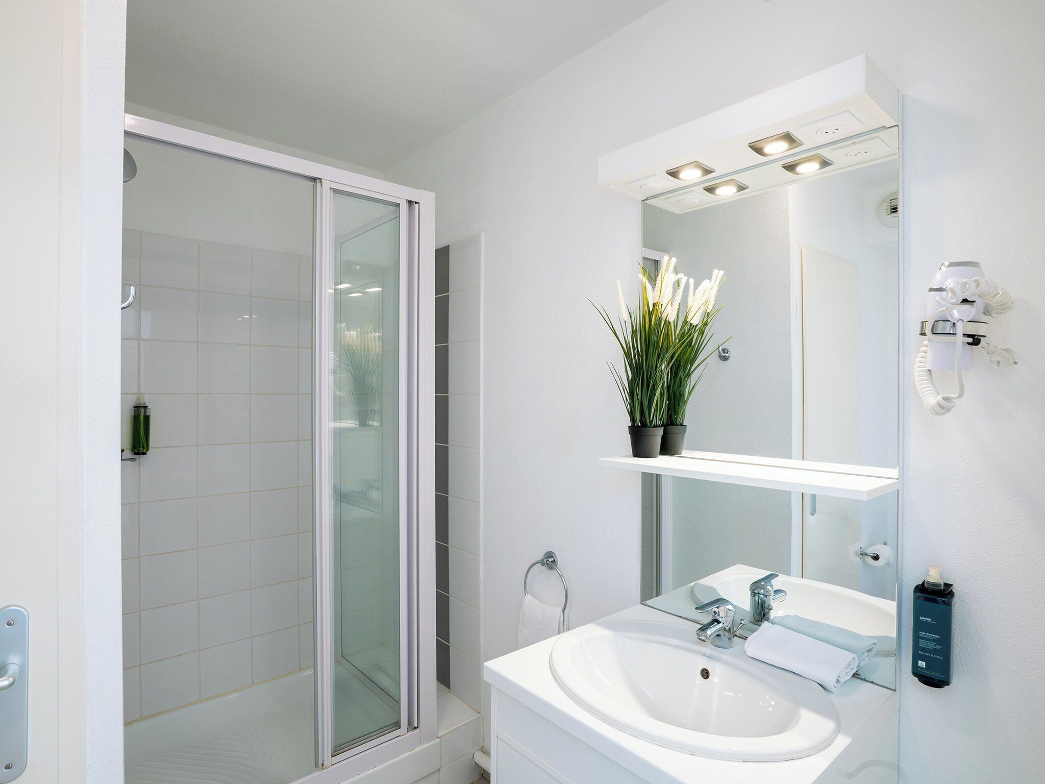 Une salle de bain moderne avec une douche à parois de verre, un lavabo blanc et un miroir doté d’un éclairage intégré.