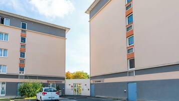 A parking lot with a white car, two buildings with beige and grey facades, and a sign for 'Les Estudines'.