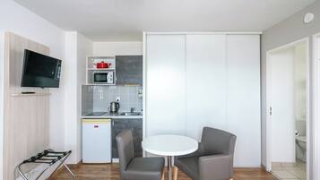 Un espacio habitable compacto con kitchenette, una zona de comedor con dos sillas, una mesa pequeña y un televisor montado en la pared.