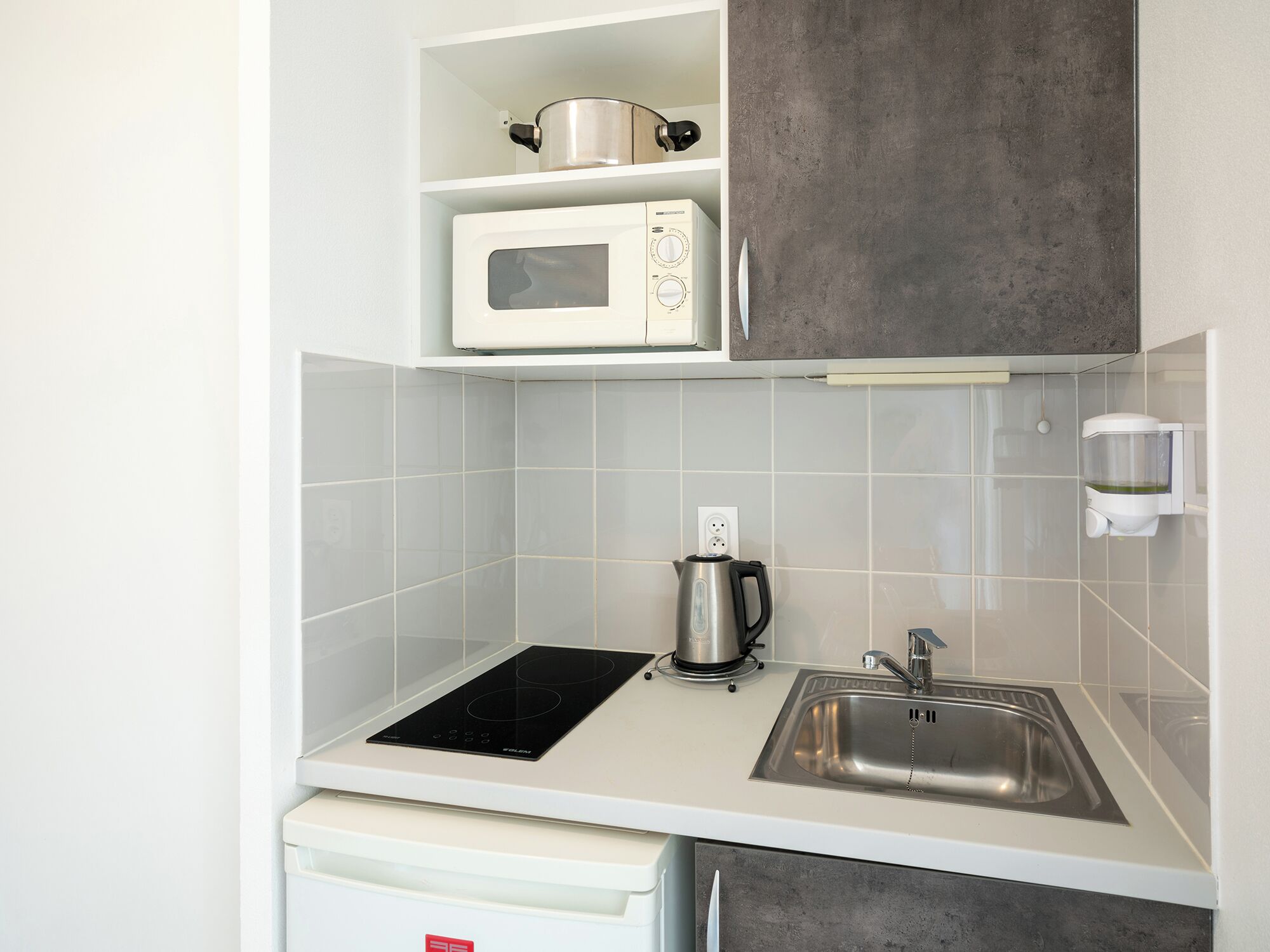 Una kitchenette compacta con microondas, tetera y pileta.