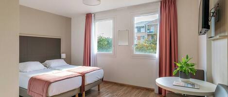 Habitación de hotel con dos camas, una mesita con una planta y una ventana con cortinas.