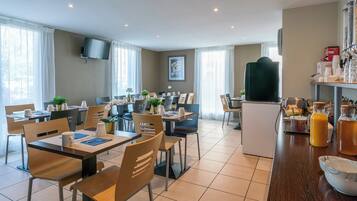 A modern hotel dining area with multiple tables and chairs, a coffee station, and a television mounted on the wall.