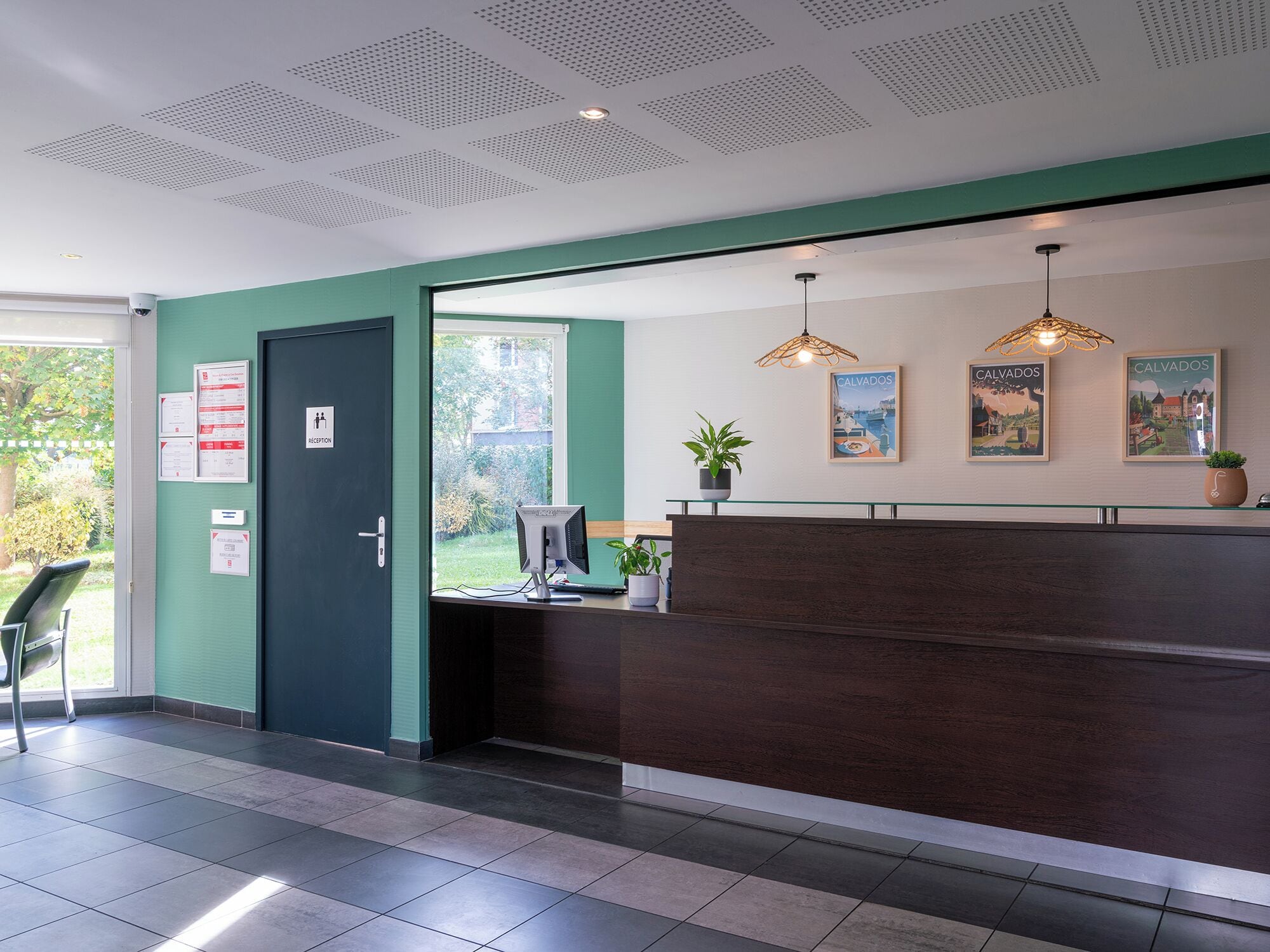 A reception area with a dark reception desk, a computer monitor, a potted plant, and two framed pictures on the wall.