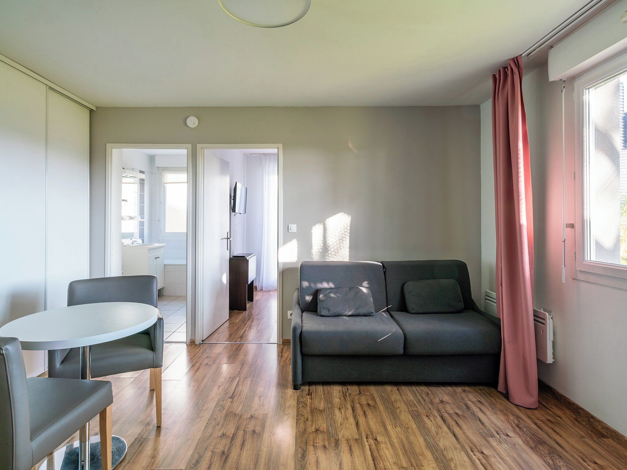 Una sala de estar moderna con un sofá gris, una mesa redonda y un televisor montado en la pared.