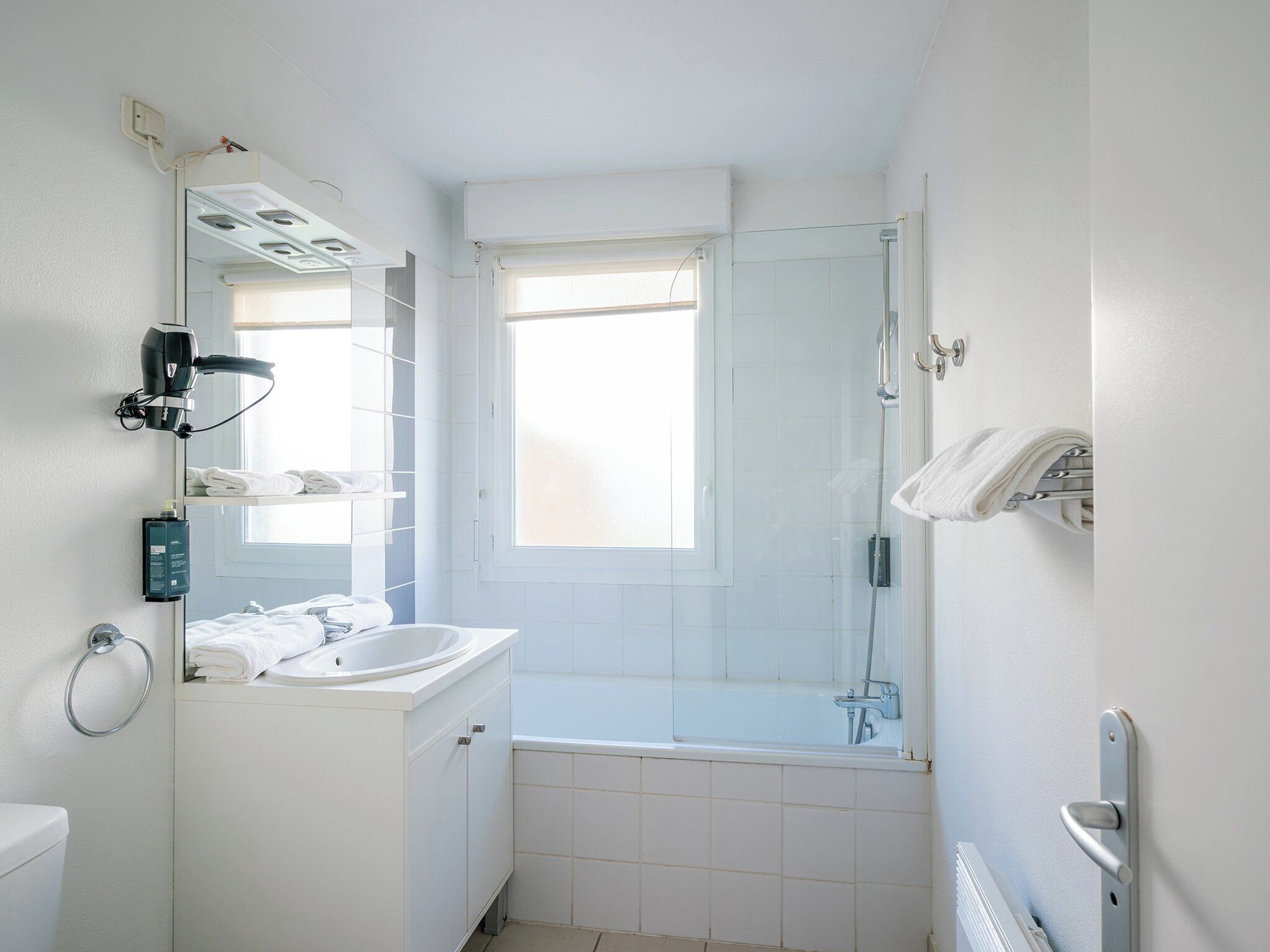 Ein kleines Badezimmer mit Waschbecken, Spiegel, Handtuchhalter und einer Duschkabine.