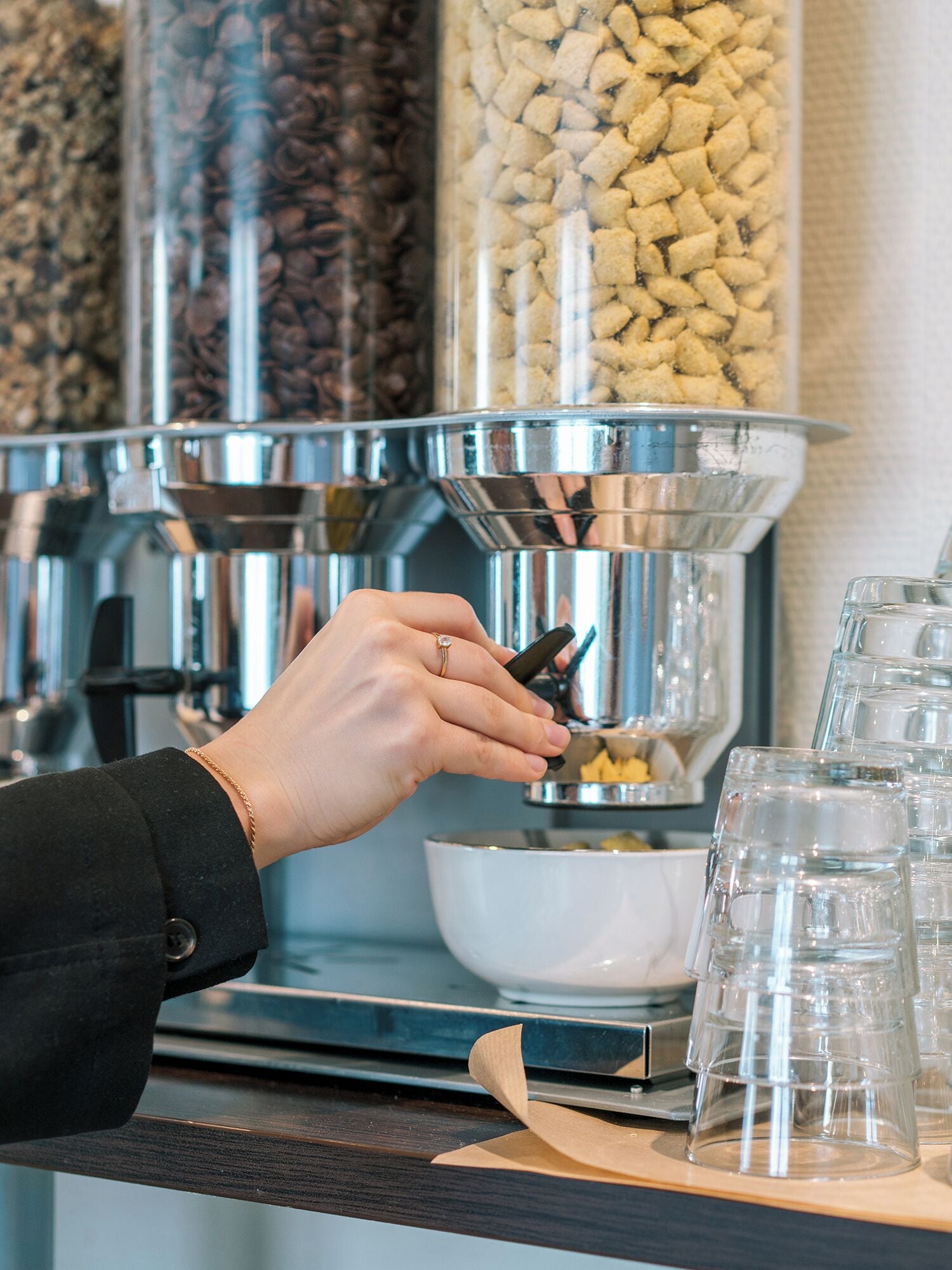 Eine Person bedient eine Kaffeemaschine, im Hintergrund ist ein Kaffeebohnen-Spender und ein Glasbehälter zu sehen.