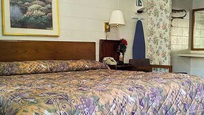 Un dormitorio con una colcha estampada, un cabecero de madera, una mesita de noche con una lámpara, un teléfono y un papel tapiz con motivos florales.