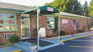 A brick building with a green awning labeled 'OFFICE,' a 'NEW MANAGEMENT LOW RATES' sign, an American flag, and a 'FREE WIFI' sign. - Relax Inn Westminster (Westminster)