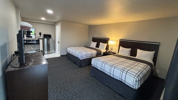A hotel room with two beds, a kitchenette, and a small bathroom.