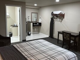 Habitación de hotel con cama, escritorio, silla, baño con espejo y lámpara colgante.